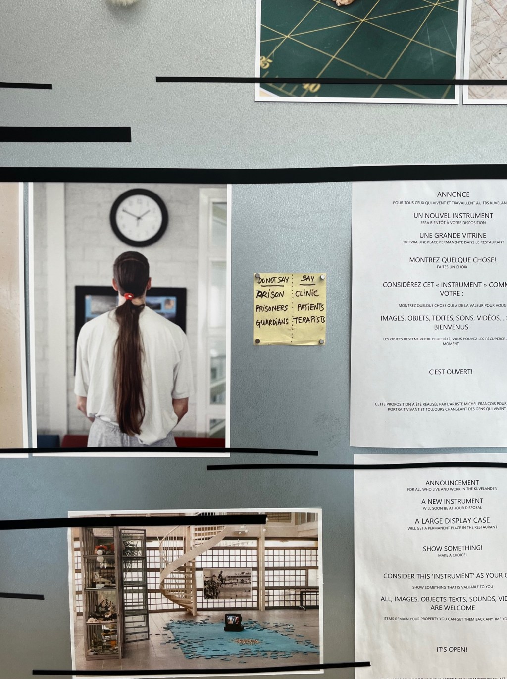 Black and white photograph of an exhibition space. On the left: photo of a scientist's back, wearing the white clinical outfit, with long dark hair. A post it note says: Do not say 'prison' 'prisoners' 'guardiands, say 'clinic' 'patients' 'terapists'.