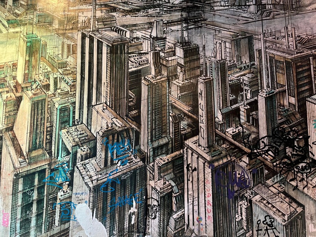 Mural of a modern metropolis with skyscrapers. Grayish-brownish colours. Some graffitis are written on the wall at the bottom of the picture.