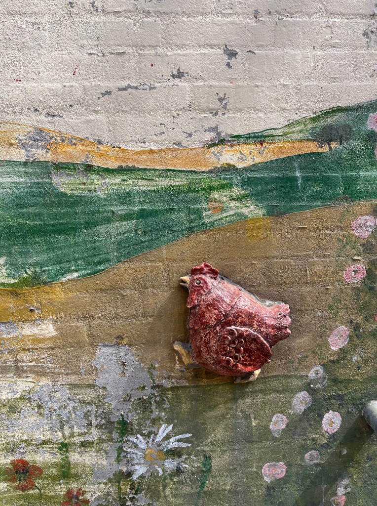 Mural painting of a chicken walking on a hill with flowers around.